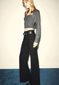 Suéter cropped de canalé gris combinado con pantalones anchos de tiro alto en negro, que cuentan con un cinturón negro grande. Texturas suaves y diseño minimalista.