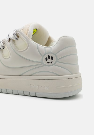 Sneaker bianco con una tomaia testurizzata, caratterizzata da una grafica fantasmatica e linee sottili. Suola spessa, accenti in bianco e nero e un logo del marchio.