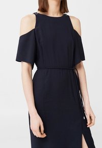 Granatowa sukienka z odsłoniętymi ramionami, krótkimi rękawami, zaciągniętym pasem w talii, bocznym rozcięciem oraz metalowymi akcentami na szwach ramion. Gładka tekstura materiału.