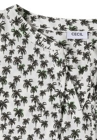 Blouse blanche avec motif de palmiers noirs et verts, col rond avec une petite fente et un lien en tissu.