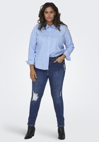 Camisa de botones a rayas azules y blancas combinada con unos jeans ajustados oscuros con detalles rasgados en las rodillas y botas negras con tobillo.