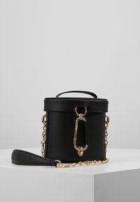 Schwarze zylindrische Tasche aus glattem Leder mit goldenen Beschlägen, einem Obertragegriff, einer Kettenriemen und einem auffälligen Verschlussdetail.