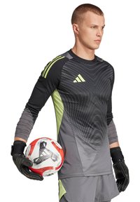 Maillot de gardien de but noir et gris avec des accents verts et un motif ondulé, associé à des gants noirs, tenant un ballon de football rouge et blanc.
