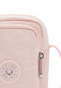 Różowa torebka na ramię z gładkiej tkaniny, wyposażona w srebrny zamek błyskawiczny oraz okrągłą naszywkę z logo. Kompaktowy design z bocznym paskiem.