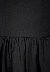 Robe noire en tissu doux et texturé, avec une taille froncée qui crée une jupe fluide. Design simple et minimaliste.