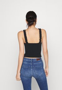 Schwarzes Tanktop mit Rüschen an den Trägern und einem quadratischen Rücken, kombiniert mit hoch taillierten blauen Jeans mit figurbetontem Schnitt und Gesäßtaschen.