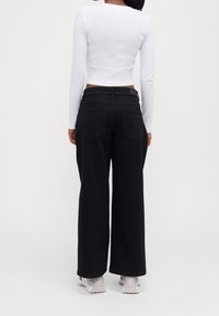 Czarne dżinsowe spodnie o szerokich nogawkach z wysokim stanem i dwoma tylnymi kieszeniami, w zestawieniu z dopasowaną białą bluzką z długim rękawem.