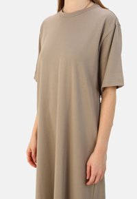 Beige oversized t-shirt dress made of soft cotton. Features set-in sleeves, a round neckline, and smooth texture. Minimalist design, no patterns.