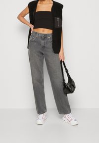 Svart ärmlös väst, kort topp och höga grå jeans. Svart handväska och vita sneakers med röda detaljer. Enkelt design, avslappnad passform.