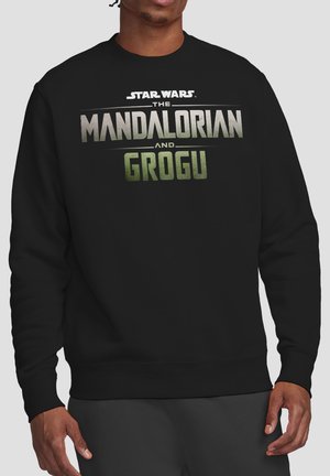 Man wearing black sweatshirt with "Star Wars The Mandalorian and Grogu" text in silver and green on chest.