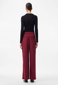 Must sõrmusega must pikakätine tops, mis on kokku sobitatud kõrge vöökoht ja laiad bordeaux' punased püksid, millel on koonusvöö ja kaks tagakotid.