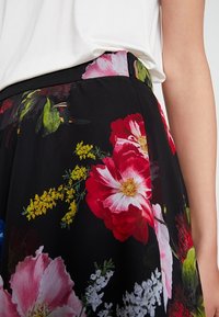 Falda negra con estampado floral que presenta grandes flores rojas y rosas con hojas verdes. Confeccionada en tejido ligero, con una textura suave y detalle en la cintura.