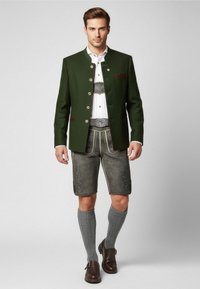 Giacca di lana verde con bottoni argentati, camicia bianca sotto, pantaloni corti grigi con ricamo, calze grigie a metà polpaccio e scarpe marrone scuro.