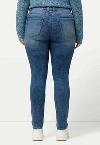 Jeans ajustados de rayas azules con una cintura de altura media, que cuentan con dos bolsillos traseros y un diseño ceñido, combinados con zapatillas blancas.