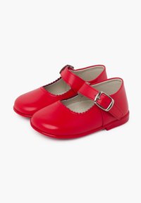 Zapatos Mary Jane de cuero rojo con puntera redondeada, bordes ondulados y una correa ajustable con hebilla. Suela plana con textura suave.