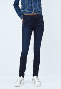 Tunna mörkblå jeans gjorda av denimtyg, med fem fickor, knäppning och dragkedja, samt en jämn yta.