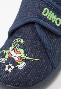 Marine textielschoen met een dinosaurusborduursel in groen en oranje, die een dinosaurus afbeeldt die voetbal speelt, voorzien van een klittenbandsluiting.