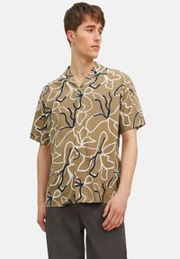 Chemise à col, à manches courtes, de couleur marron avec un motif floral en bleu marine et blanc, fabriquée en tissu léger. Dotée de boutons sur le devant.