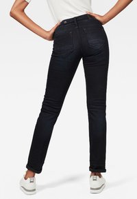 Svarta smala jeans med medelhög midja, bakfickor och en slät denimtextur, parat med vita sneakers.