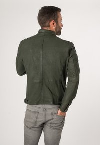 Olijfgroen leren motorjack met een getailleerde silhoutte, schouderaccenten en detailwerk op de achterkant. Gecombineerd met grijze jeans.