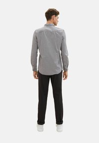Chemise �à carreaux noire et blanche, à manches longues, avec col boutonné, ourlet droit, portée avec un pantalon foncé et des baskets blanches.