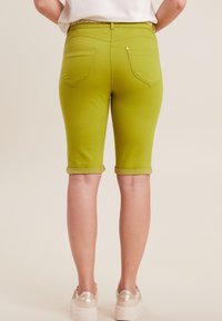 Grüne Jeansshorts mit umgeschlagenen Säumen, ausgestattet mit zwei Gesäßtaschen und silberfarbenen Beschlägen. Der Stoff wirkt glatt und dehnbar.
