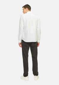 Camisa blanca de manga larga con cuello, combinada con pantalones gris oscuro y zapatillas blancas. La camisa presenta una textura suave y puños con botones.