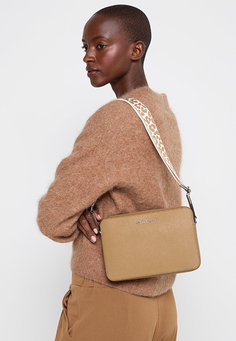 Sac en cuir brun clair en bandoulière de forme rectangulaire, avec une surface texturée et une bandoulière à imprimé léopard. Logo de la marque visible.