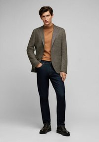Grau karo-blazer über einem braunen Rollkragenpullover, kombiniert mit dunklen Denimjeans und schwarzen Schnürschuhen. Einfaches Design, strukturierte Passform.