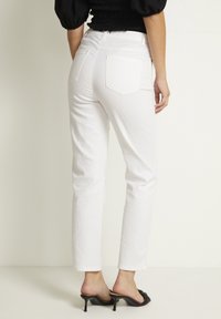 Jeans de mezclilla blanca con pierna recta, dos bolsillos traseros y dobladillo vuelto, combinados con mulas negras de tacón. La textura parece suave.