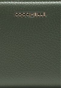Portefeuille en cuir texturé vert foncé avec le logo "COCCINELLE" en relief doré à l'avant.
