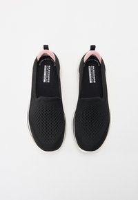 Sapatos pretos tipo slip-on com um superior de malha respirável, acabamentos em rosa na parte de trás e uma sola branca. Apresenta almofadamento Goga Mat para conforto.