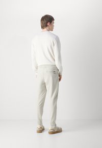 Pantalons beige clair avec poignets élastiques et taille à cordon, associés à un haut à manches longues blanc, vue de dos, design minimaliste.