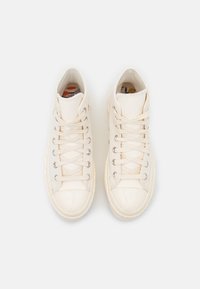 Para białych wysokich trampków z płóciennym wierzchem, białymi sznurowadłami, metalowymi oczkami i dekoracyjnymi, wielokolorowymi wzorami wewnątrz podszewki.