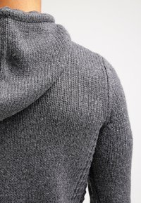 Grauer gestrickter Kapuzenpullover mit texturierter Oberfläche und weichem Stoff. Verfügt über eine lässige Kapuze und sichtbare Nähte entlang der Säume.