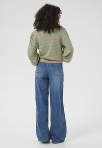 Maglione a righe beige con strisce verdi, abbinato a jeans in denim blu a gamba larga. Design in maglia con texture e vestibilità rilassata.