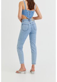 Top corto de mezclilla con tirantes ajustables, espalda descubierta y vaqueros de tiro alto en azul claro. Modelo lleva sandalias de tacón cuadrado grises.