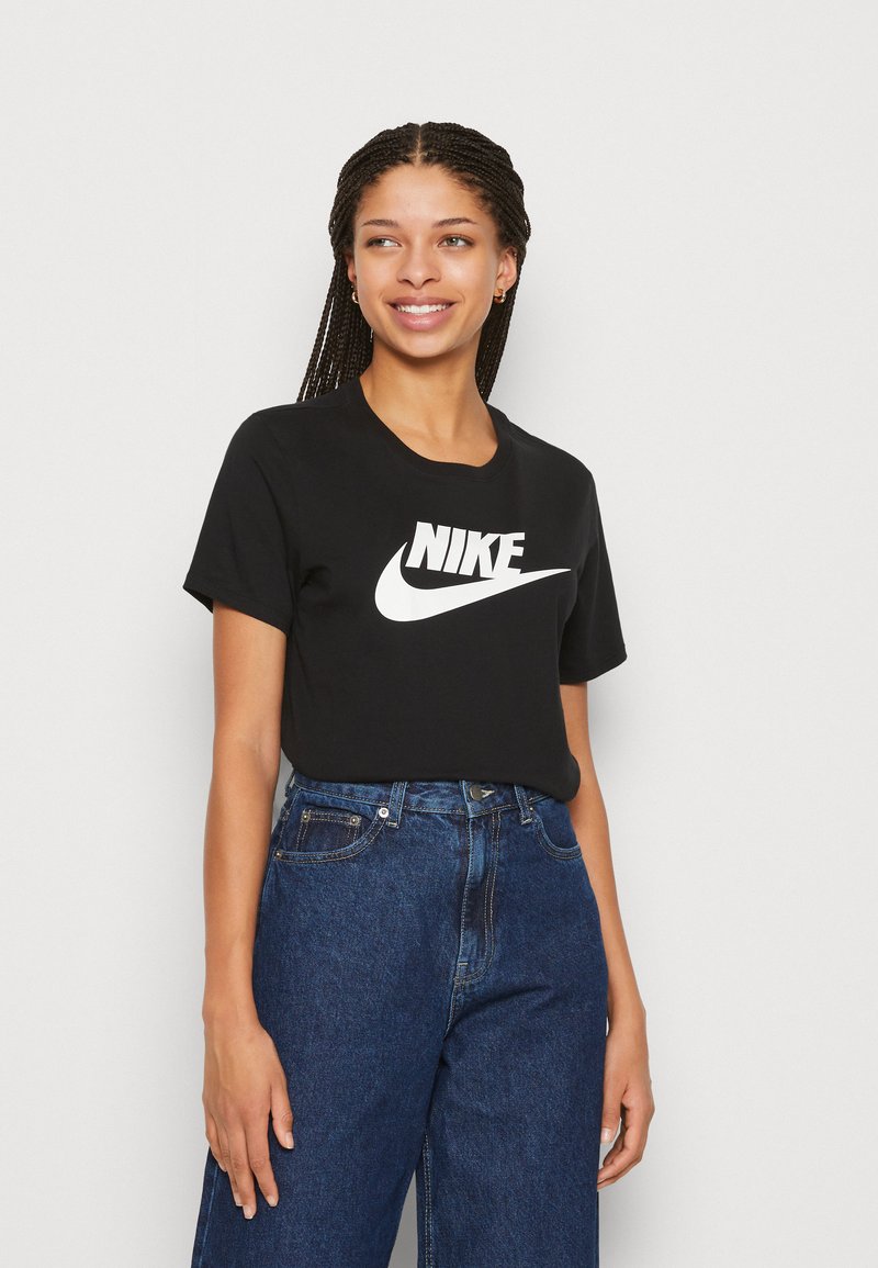 Zwarte katoenen t-shirt met een groot wit Nike-logo, gecombineerd met hooggebreuseerde blauwe denim jeans. Het shirt heeft een ronde hals en korte mouwen.