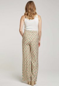 Pantalon à jambes larges avec un motif géométrique vert, rose et blanc. Taille élastique, tissu léger. Le modèle porte un débardeur blanc.