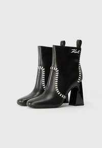 Bottines en cuir noir à talon carré. Caractérisées par des accents de couture blanche et une boucle à l'arrière. Détail du logo sur le côté en blanc.