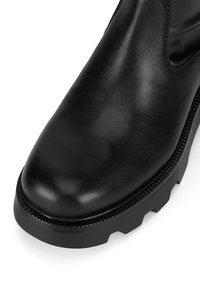 Botín negro de cuero con punta redondeada, paneles laterales texturizados y una suela gruesa de goma con acentos estriados.