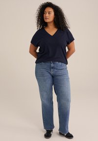 Marinblå kortärmad V-ringad topp med texturmönster, kombinerad med blå raka jeans och svarta sneakers. Enkelt, avslappnat outfit.