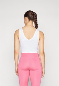 Top cropped branco sem mangas com costas em V, combinado com leggings rosa de cintura alta com uma textura suave e costuras contrastantes.