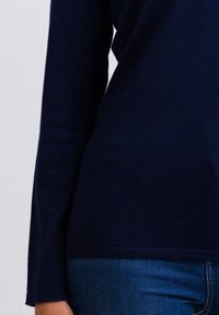 Maglietta a maniche lunghe blu navy realizzata in materiale morbido, design aderente con una texture liscia, abbinata a jeans blu visibili sul fondo.