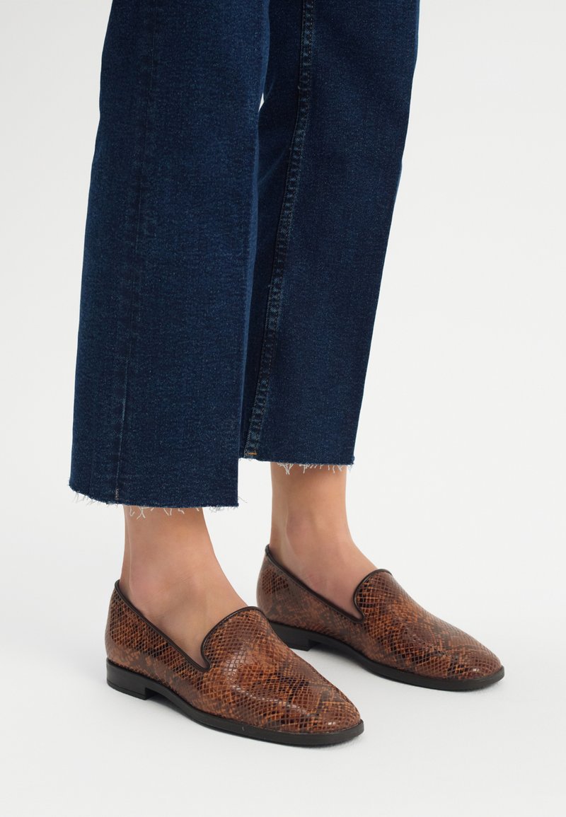 Bruine loafers met slangenprint, met een gladde textuur en een puntige neus, gecombineerd met donkerblauwe cropped jeans met rafelige zomen.