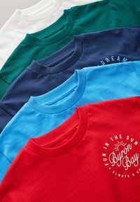 Cinq t-shirts à col rond pliés en blanc, vert, bleu foncé, bleu clair et rouge, avec le texte « Byron Bay » et un graphique de soleil sur le rouge.