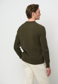 Mörkgrön ribbade tröja med långa ärmar och rund halsringning, med figursydd midja och strukturerat stickat mönster, bärs över krämfärgade byxor.