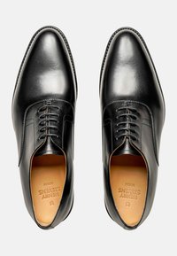 Schwarze Leder-Oxfords mit elegantem Design, spitz zulaufender Zehenpartie und Schnürung vorne sowie dezentem Stitching. Das Innenfutter ist beige.