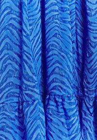 Blå klänning med ett texturerat zigzagmönster, gjord av lättviktsmaterial. Har volangsektioner och en slät yta.