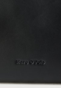 Zwarte leren handtas met een gestructureerd oppervlak. Voorzien van het geperste "Marc O'Polo" logo aan de onderkant. Compact rechthoekig ontwerp.